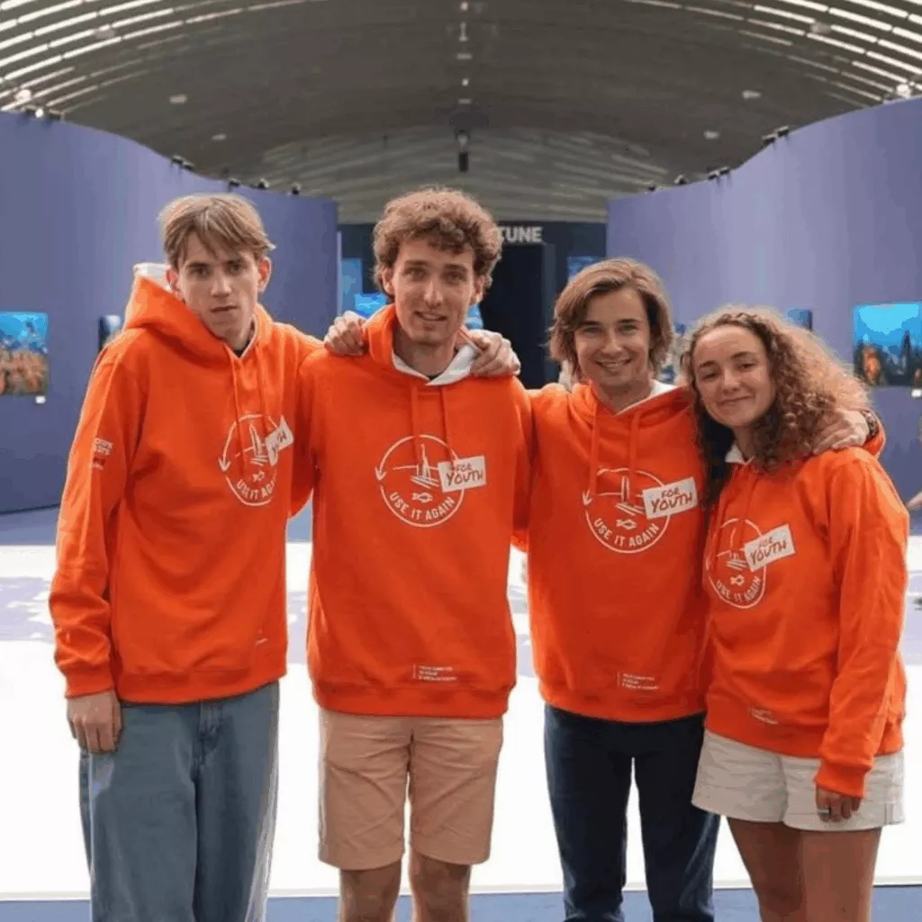 Quatre jeunes en sweats orange Use It Again for Youth posent dans une exposition, lors de l'UNOC à Nice